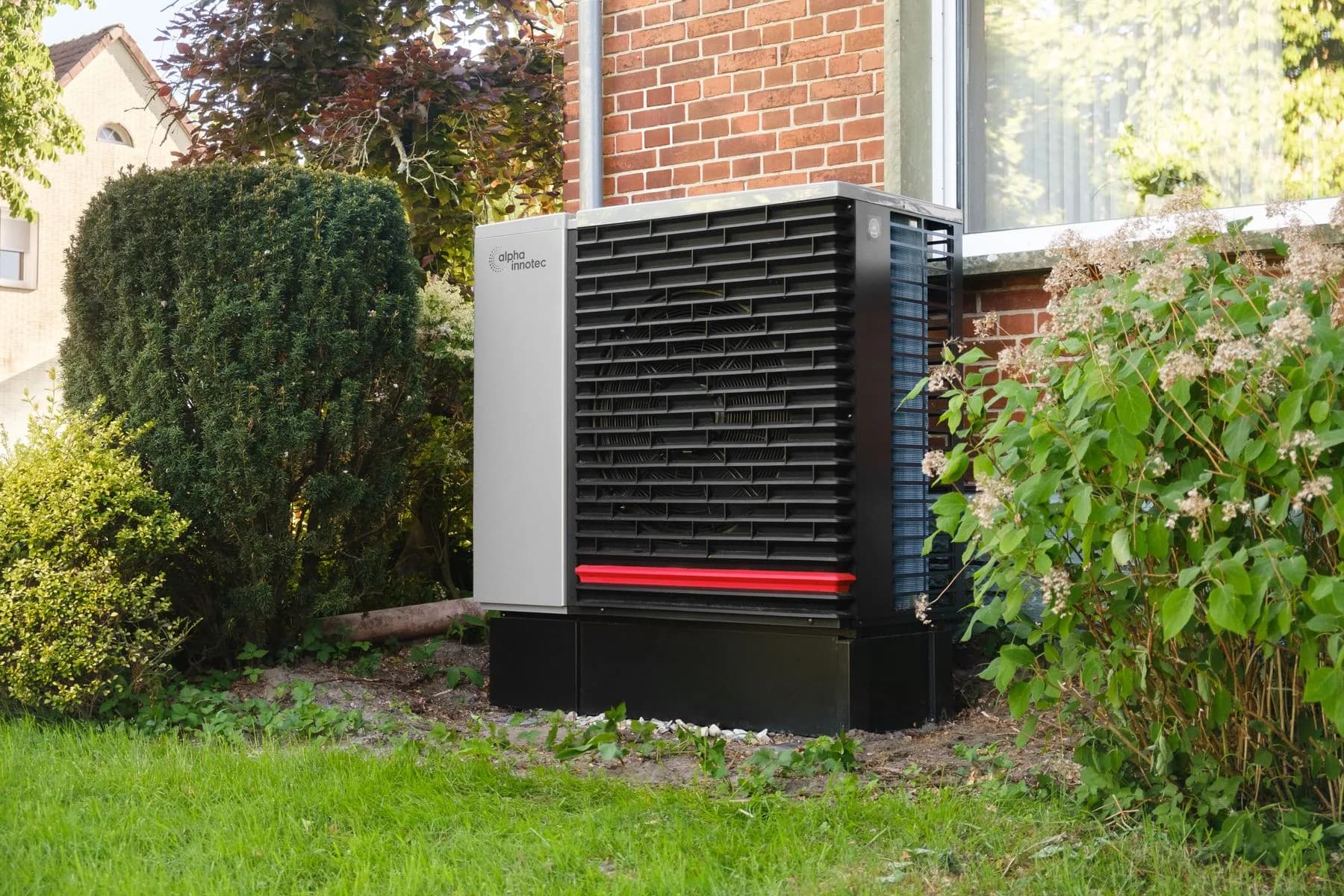 Moderne Luftwärmepumpe im Garten eines Wohnhauses